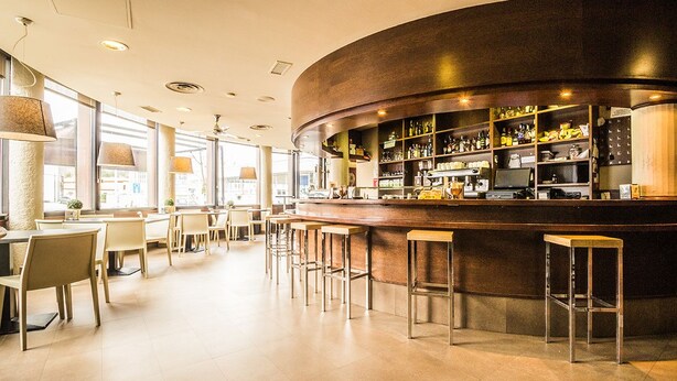 A modern bar area with a curved counter, bar stools, and a well-lit interior. - Casa Jacinto Pamplona  (Burlada)