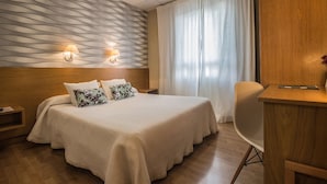 A hotel room with a large bed, two wall-mounted lamps, a wooden headboard, a wooden desk, and a chair. - Casa Jacinto Pamplona  (Burlada)