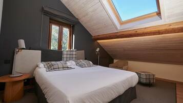Un dormitorio con tragaluz, una cama con ropa de cama escocesa, una mesita de noche con lámpara y un pequeño otoman.