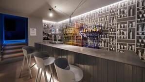 Uma área de bar com um balcão comprido, vários bancos e prateleiras cheias de garrafas e copos.