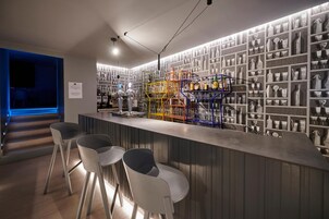 A bar area with a long counter, multiple stools, and shelves filled with bottles and glasses.