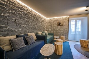 A modern living room with a stone wall, a blue sofa, a green armchair, and round wooden tables.