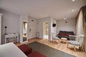 Una sala de estar moderna con un sofá, un escritorio con una silla, un televisor montado en la pared y una puerta que da a otra habitación.