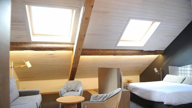 Quarto estilo loft moderno com teto inclinado, claraboias, uma cama, um sofá e uma pequena mesa redonda.