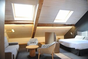 A modern loft bedroom with a sloped ceiling, skylights, a bed, a sofa, and a small round table.