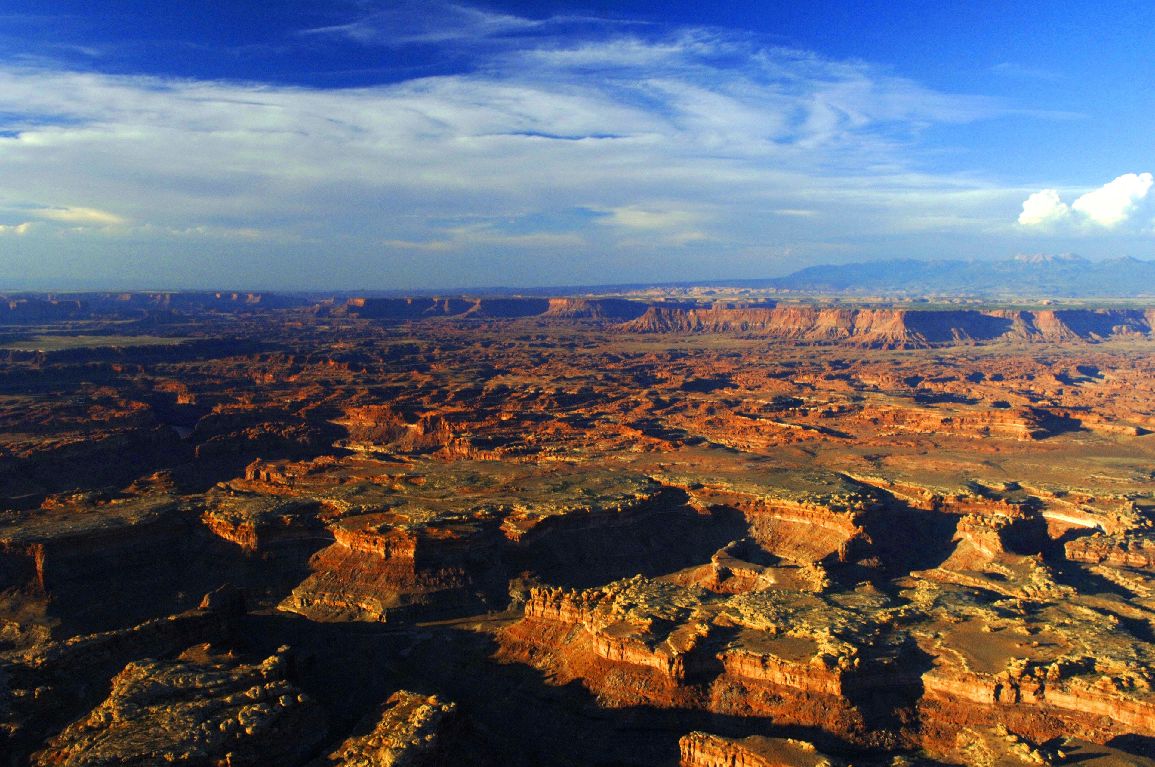 A vast canyon landscape with rugged terrain and distant mountain ranges.