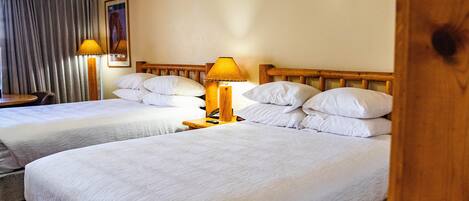 Camera d'albergo con due letti, una testiera in legno, un comodino con una lampada e una ventola a soffitto.