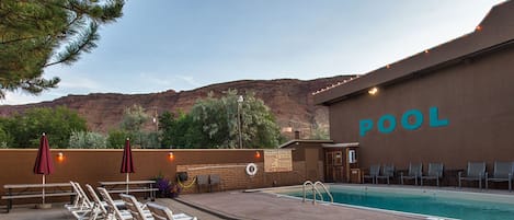 A pool area with lounge chairs, a sign indicating no diving, and a view of a mountain range.