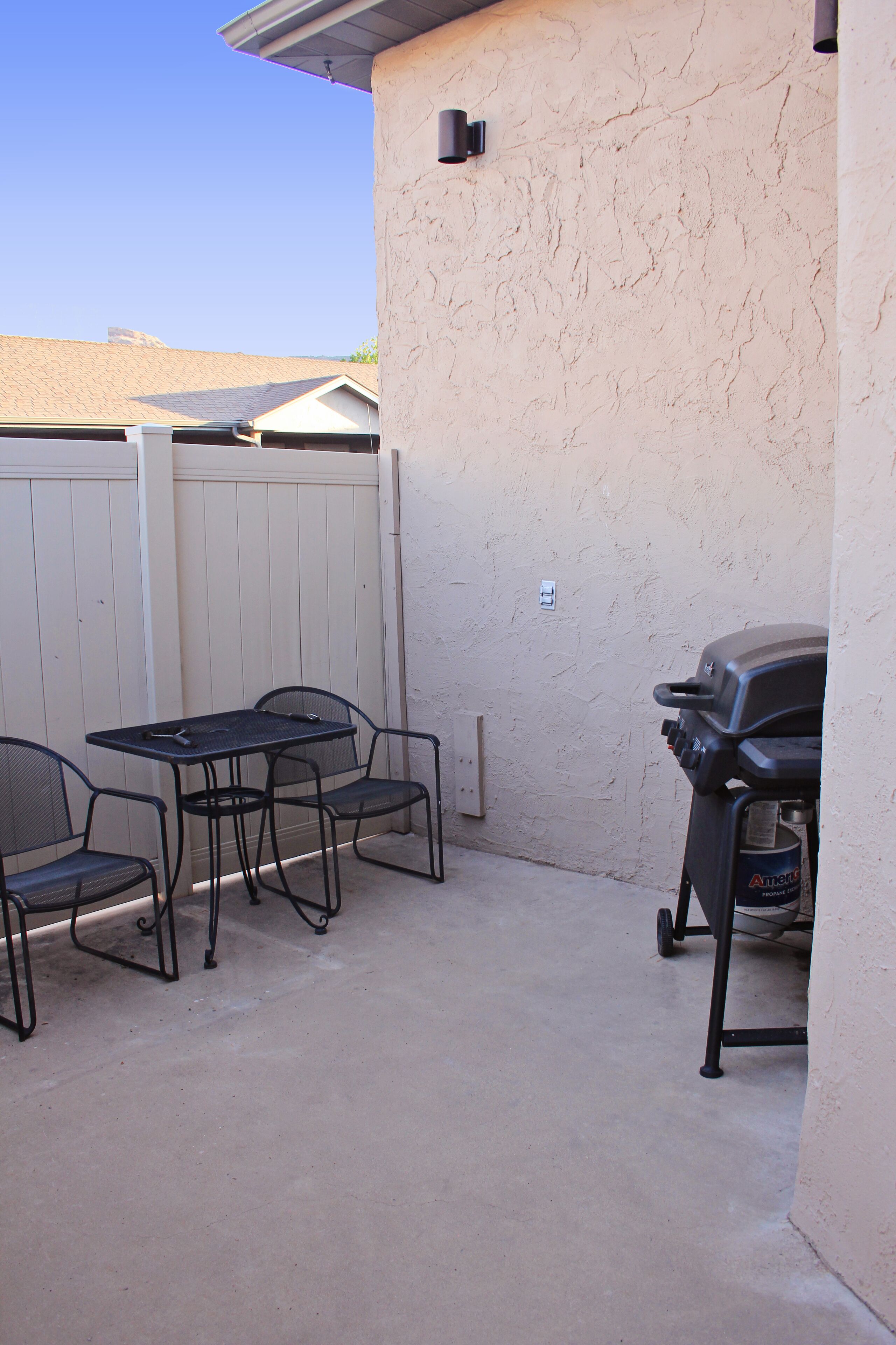 Un patio al aire libre con una mesa, sillas, una parrilla y una cerca blanca.
