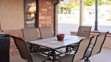 An outdoor patio with a table and chairs, a trash can, and a brick wall.