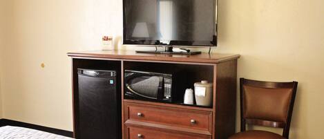A hotel room with a bed, a wooden dresser with a television, a microwave, and a chair.