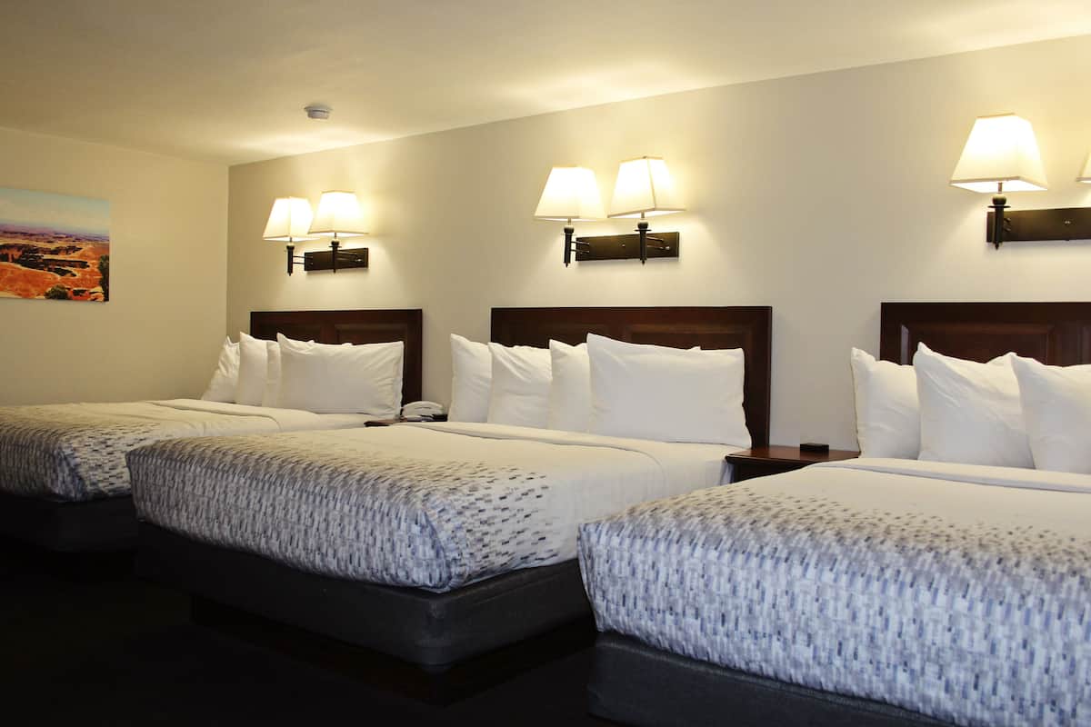 A hotel room with three single beds, each with a headboard, bedside tables, and lamps.