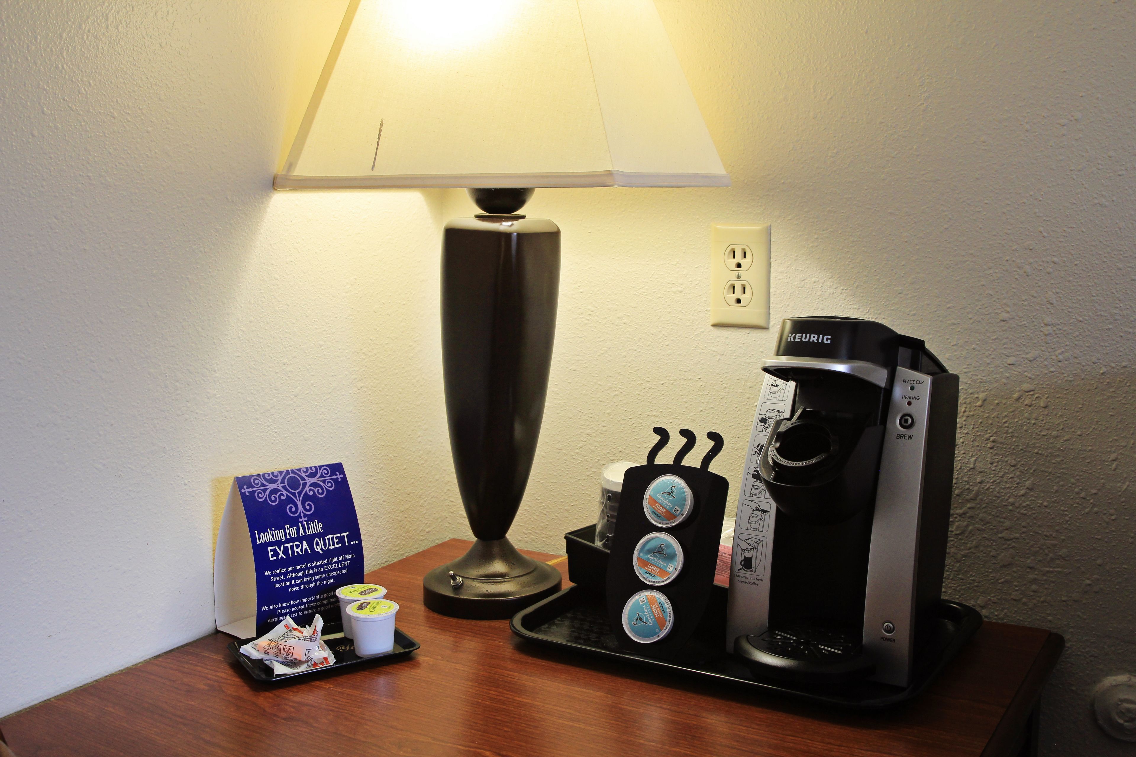 A coffee maker with a Keurig brand, a tray with coffee pods, a small cup, and a sign about extra quiet.