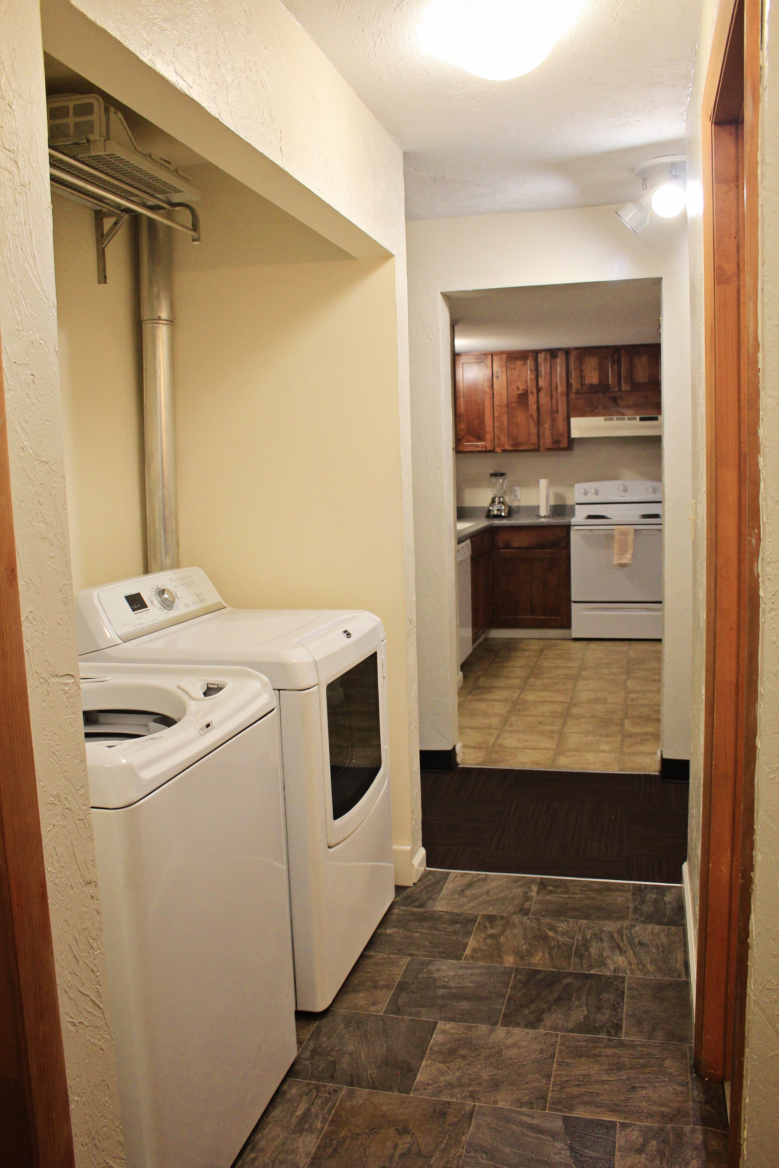 A laundry area with two washing machines and a dryer, a kitchen with wooden cabinets and a stove, and a tiled floor.