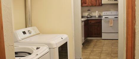 A laundry area with two washing machines and a dryer, a kitchen with wooden cabinets and a stove, and a tiled floor.