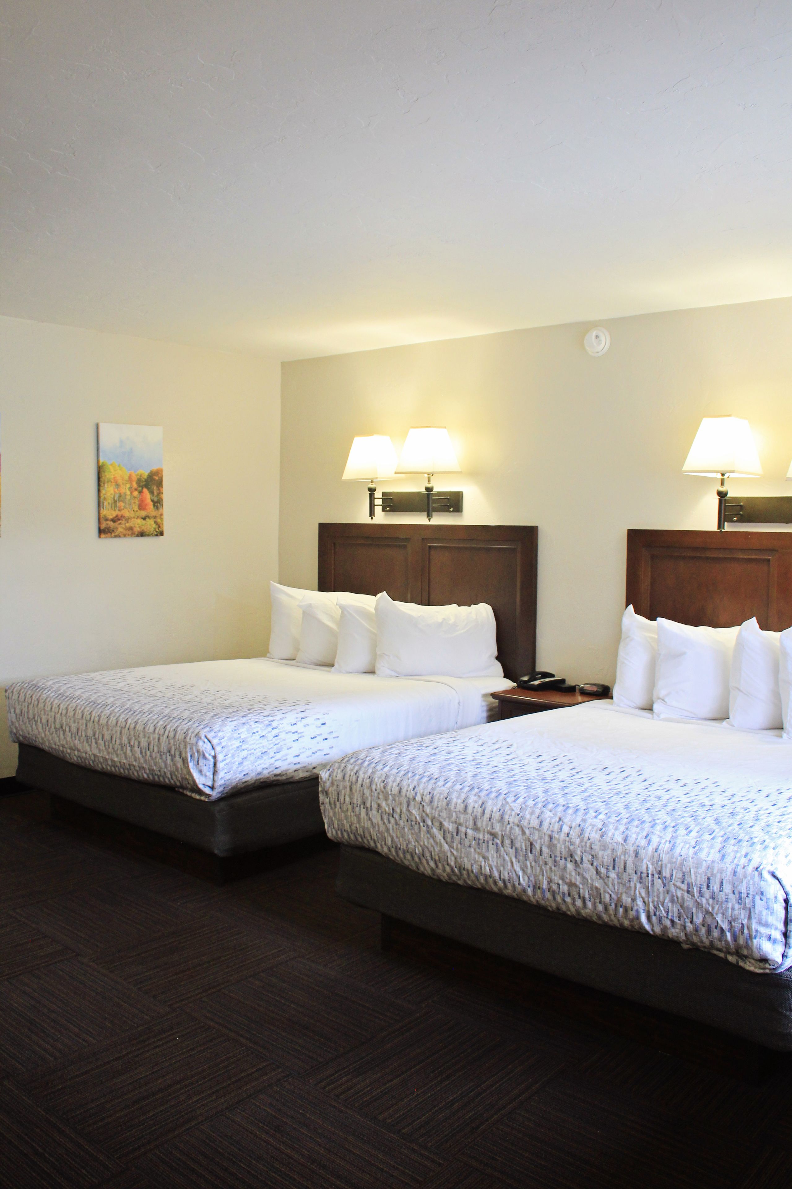 A hotel room with two beds, each with a wooden headboard, white bedding, and bedside lamps.