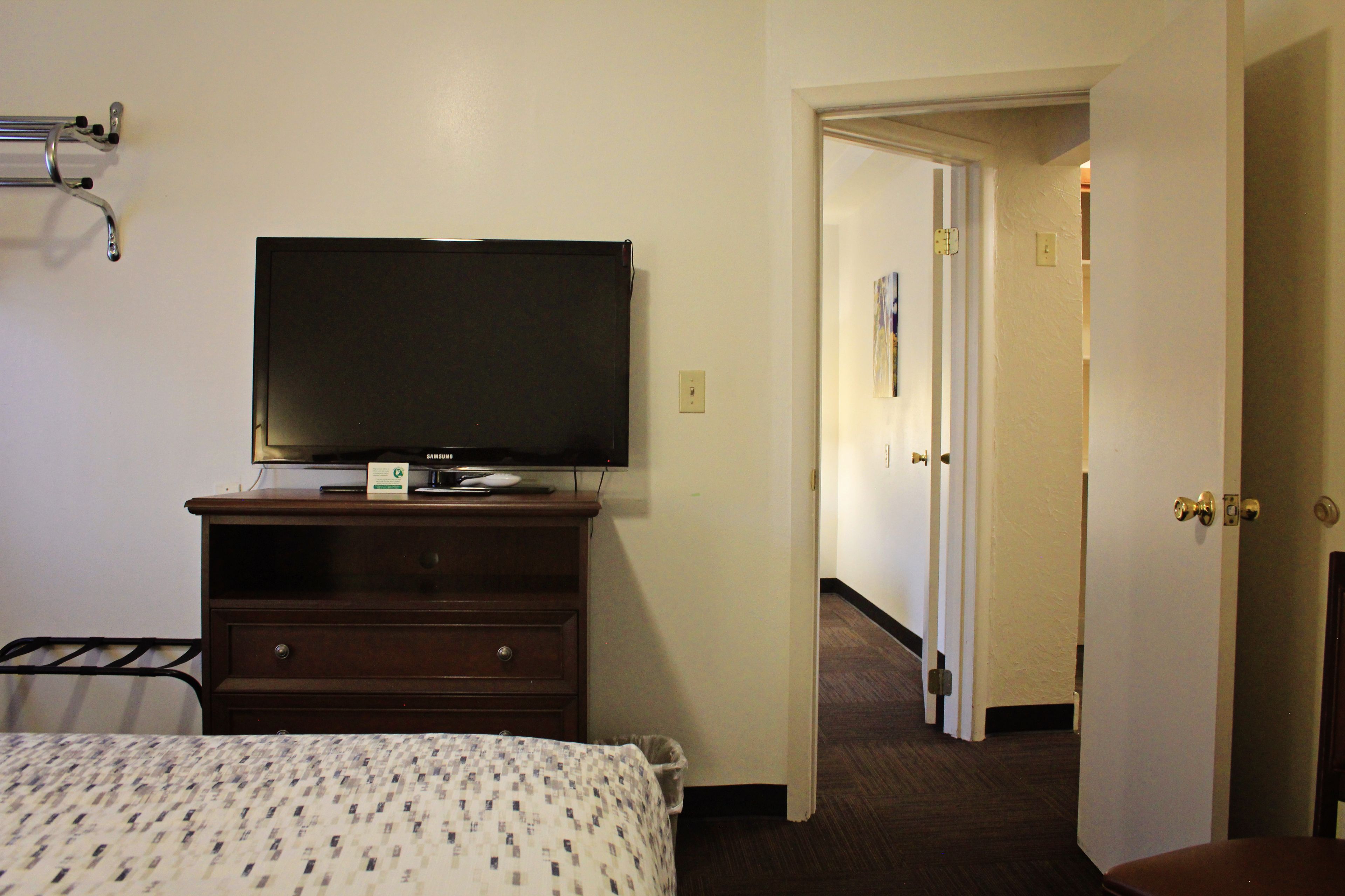 Une chambre d’hôtel avec un lit, un téléviseur posé sur une commode, une porte donnant sur une autre pièce et un couloir.