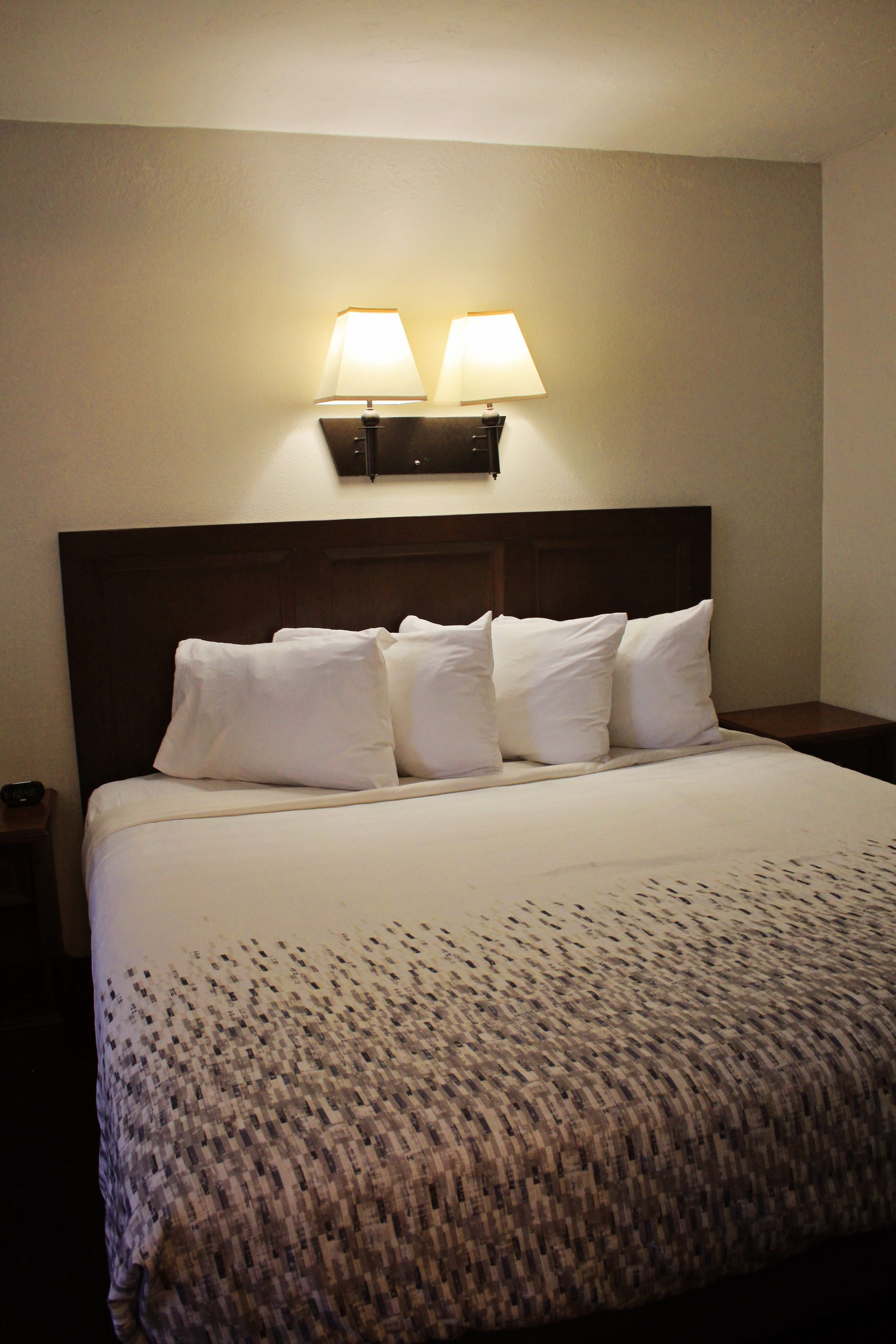 A neatly made bed with white linens and a textured blanket, a wooden headboard, and two wall-mounted lamps.