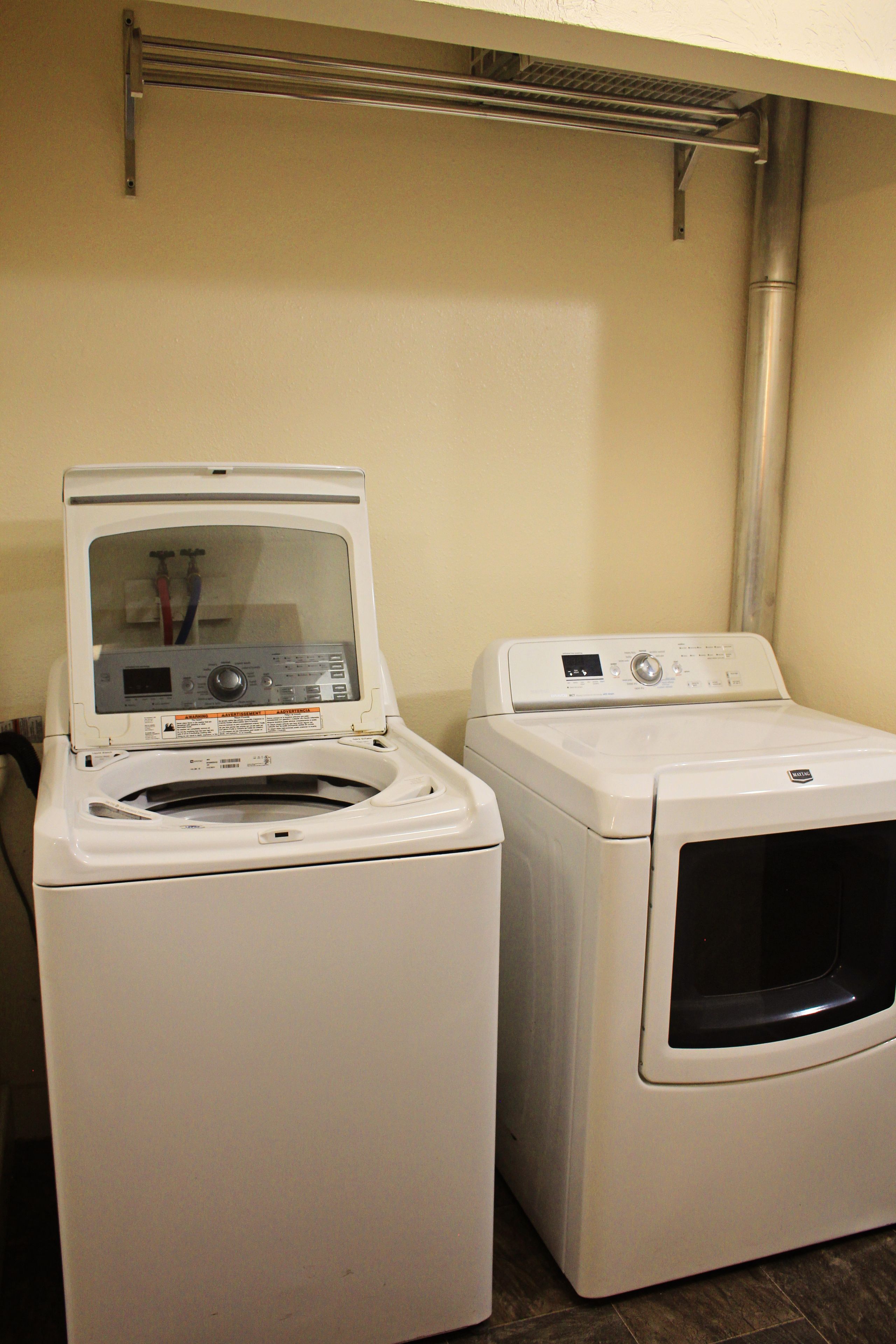Een wasruimte met twee witte wasmachines en een metalen droogrek.