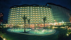 Un hotel grande de varios pisos con un patio central que cuenta con una fuente y palmeras.