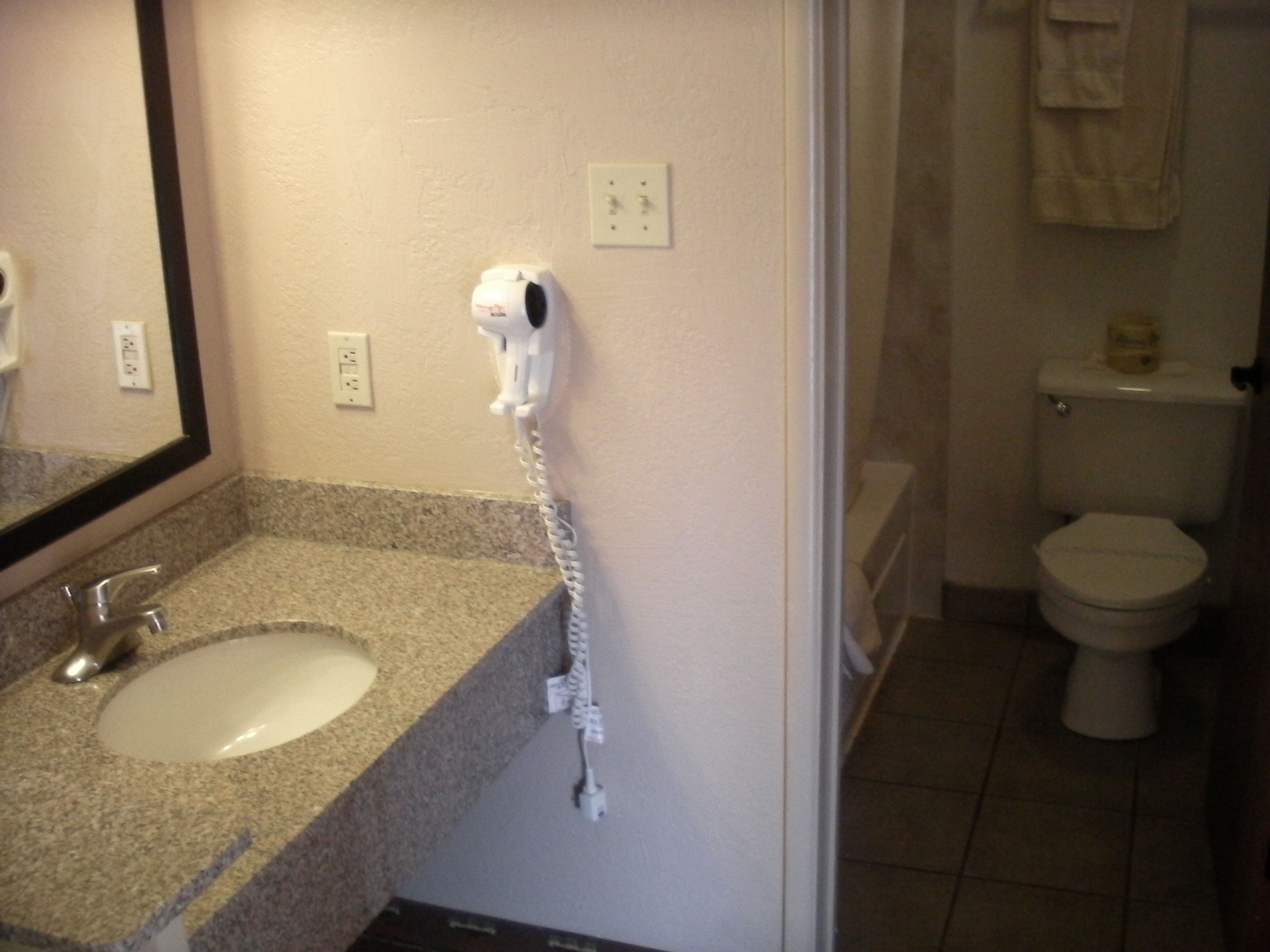 A bathroom with a sink, mirror, hairdryer, and toilet.