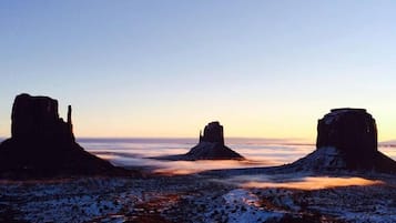 A desert landscape with three rock formations silhouetted against a sunset sky.