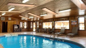 A pool area with wooden ceiling beams, a pool with a 5ft depth marker, and a sign warning of no lifeguard on duty.