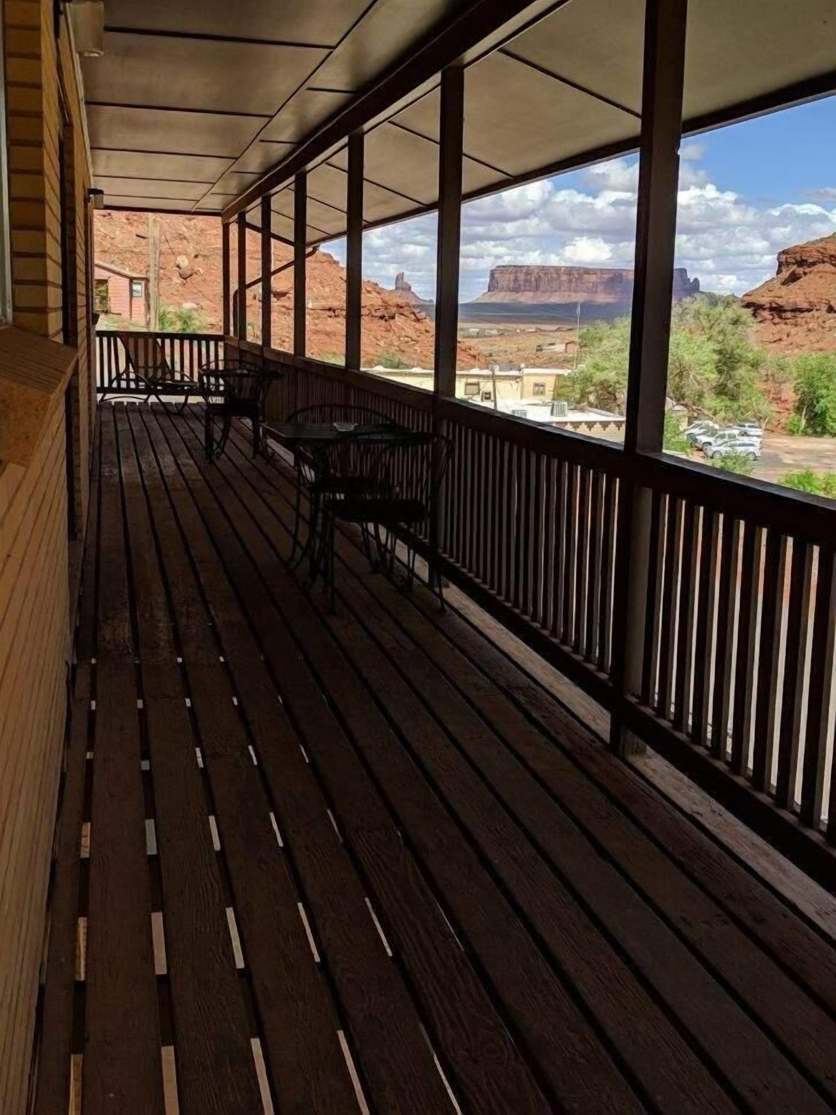Un espacio al aire libre cubierto con piso de madera, barandales de metal y vistas a formaciones rocosas rojas.