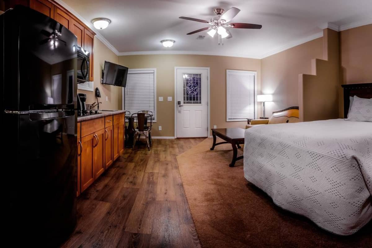 Une chambre avec un grand lit, des armoires en bois, un ventilateur de plafond et un téléviseur.