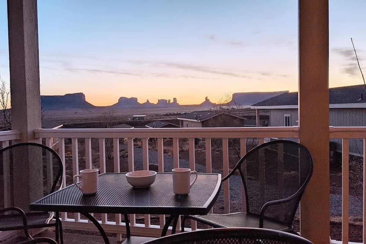 Un balcon avec une table et des chaises, offrant une vue panoramique sur un paysage désertique caractérisé par des formations rocheuses remarquables.