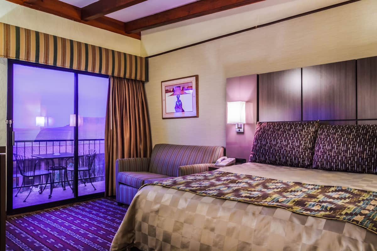 Une chambre d’hôtel avec un lit, un canapé, une petite table et un balcon équipé de chaises.