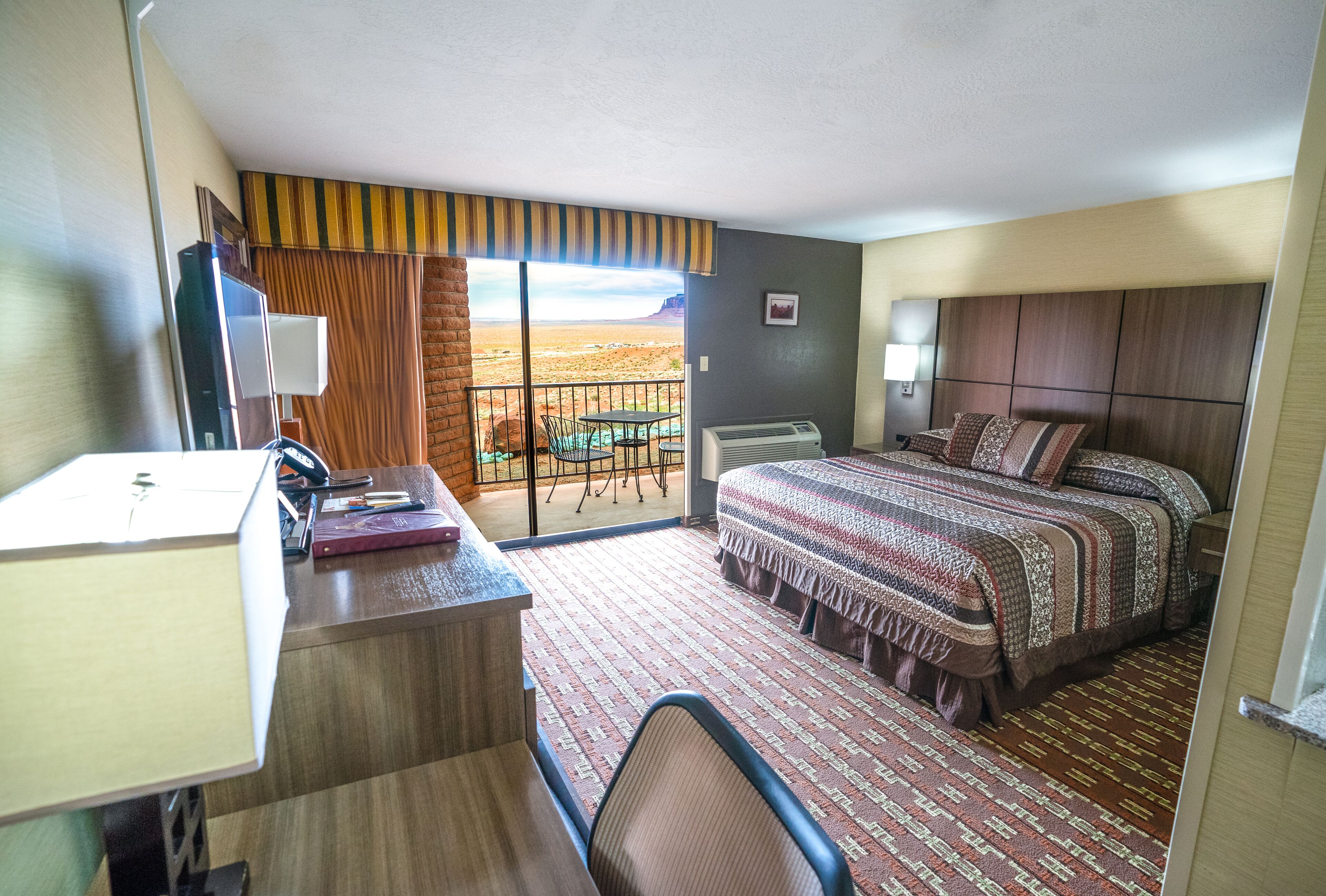 Habitació d'hotel amb escriptori, llit, vista a un paisatge desèrtic i un balcó amb taula i cadires.