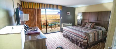 Habitación de hotel con escritorio, cama, vista a paisaje desértico y balcón con mesa y sillas.