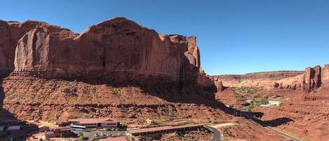 A desert landscape with a prominent rock formation and a building complex with multiple structures and a parking area.