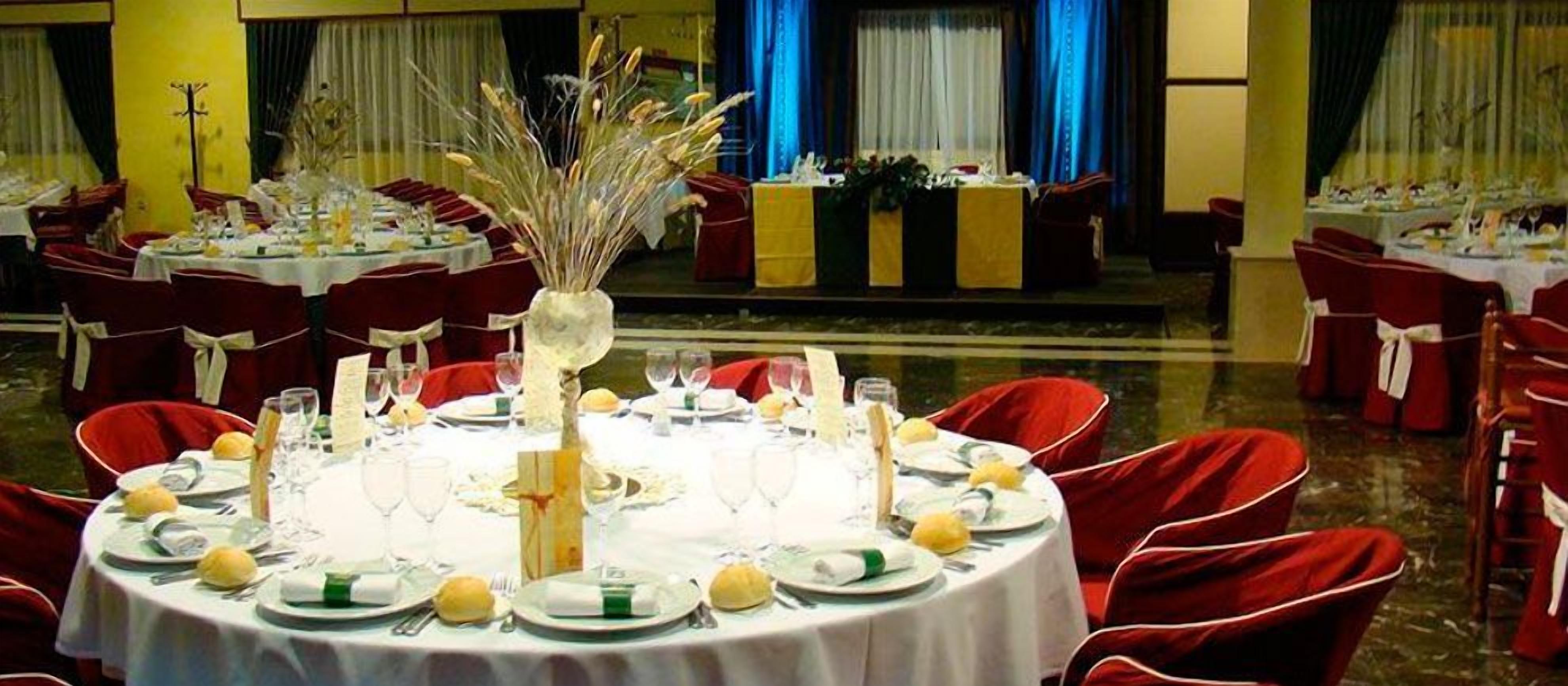 Un salón de banquetes con mesas redondas dispuestas para un evento formal, con manteles blancos, sillas rojas y centros de mesa florales.