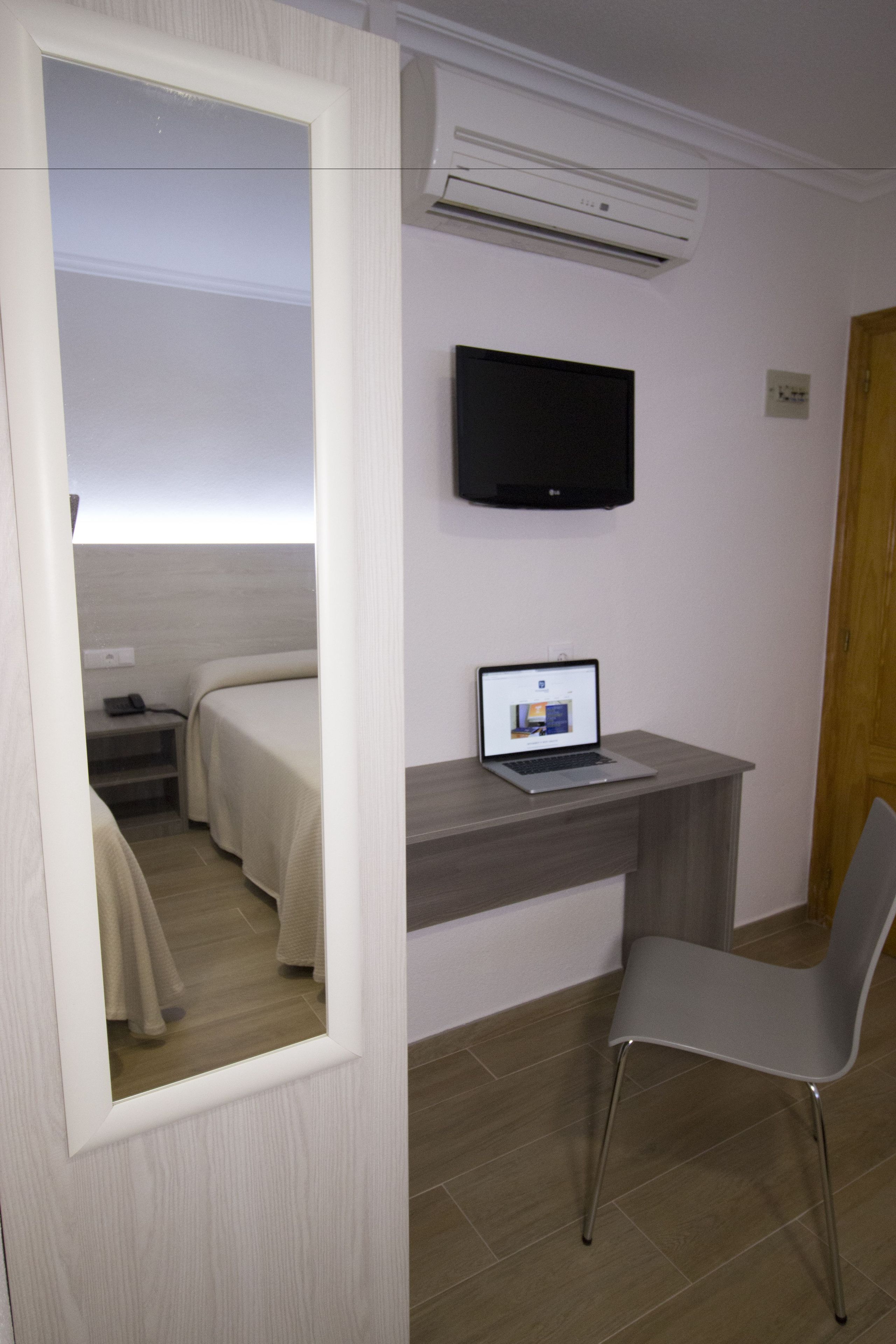 Quarto de hotel com cama, escrivaninha com laptop, televisão e ar condicionado.