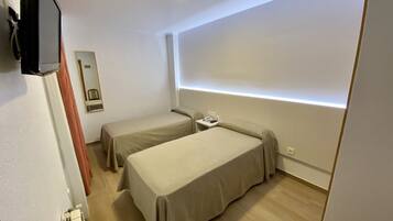 Une petite chambre moderne, équipée de deux lits simples, d’une table de chevet avec un téléphone et d’un téléviseur à écran plat fixé au mur.