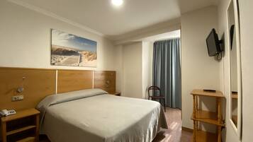 A hotel room with a bed, a nightstand, a TV mounted on the wall, a window with curtains, and a painting on the wall.