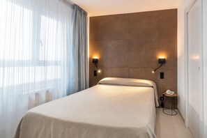 A modern hotel room with a large bed, two wall-mounted lights, a telephone, and a small side table. - Hostal Pensimar (Elche)