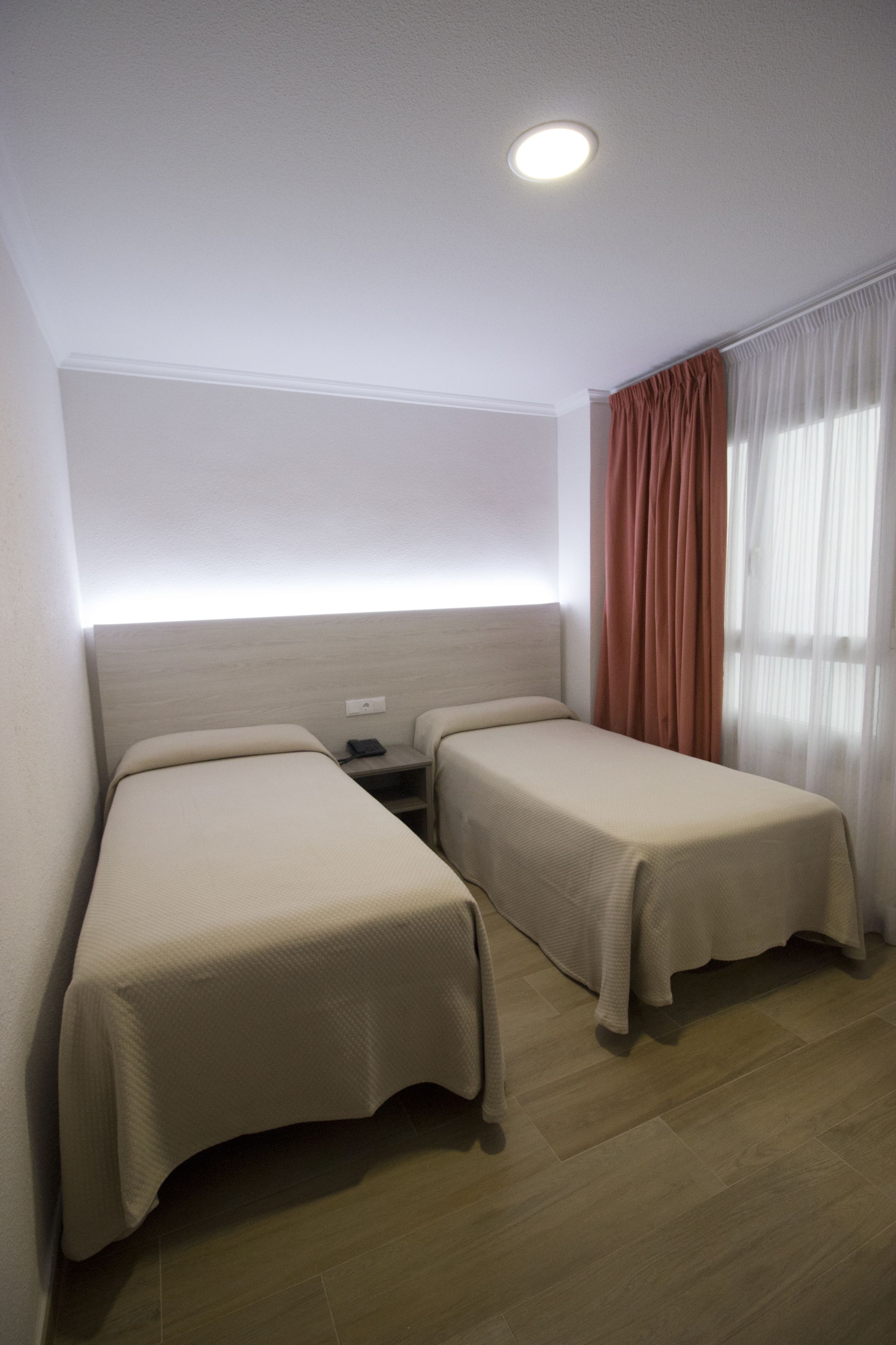 A hotel room with two single beds, a nightstand, a phone, and a window with curtains.