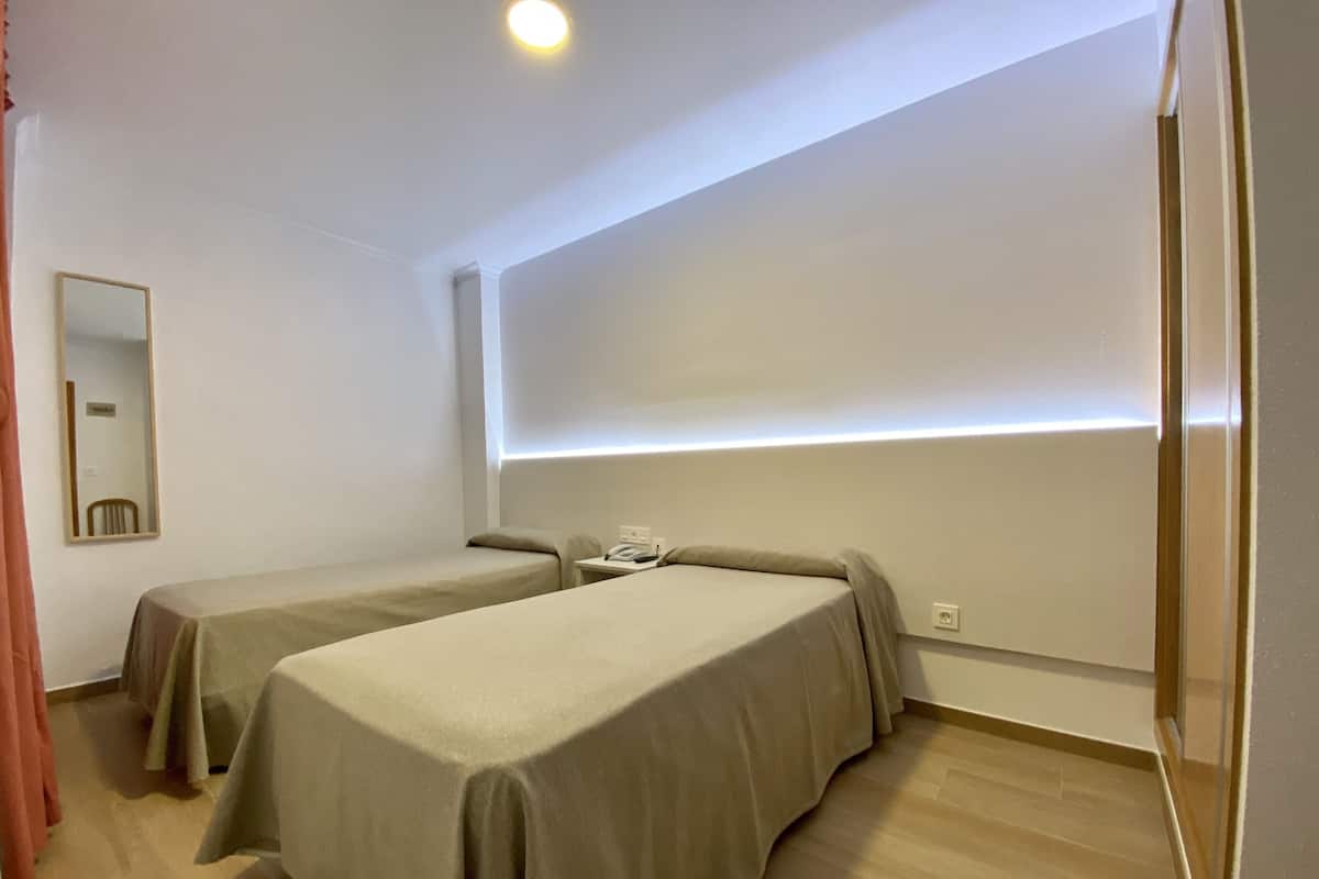 A hotel room with two single beds, a bedside table with a phone, a mirror, and a light strip along the ceiling.