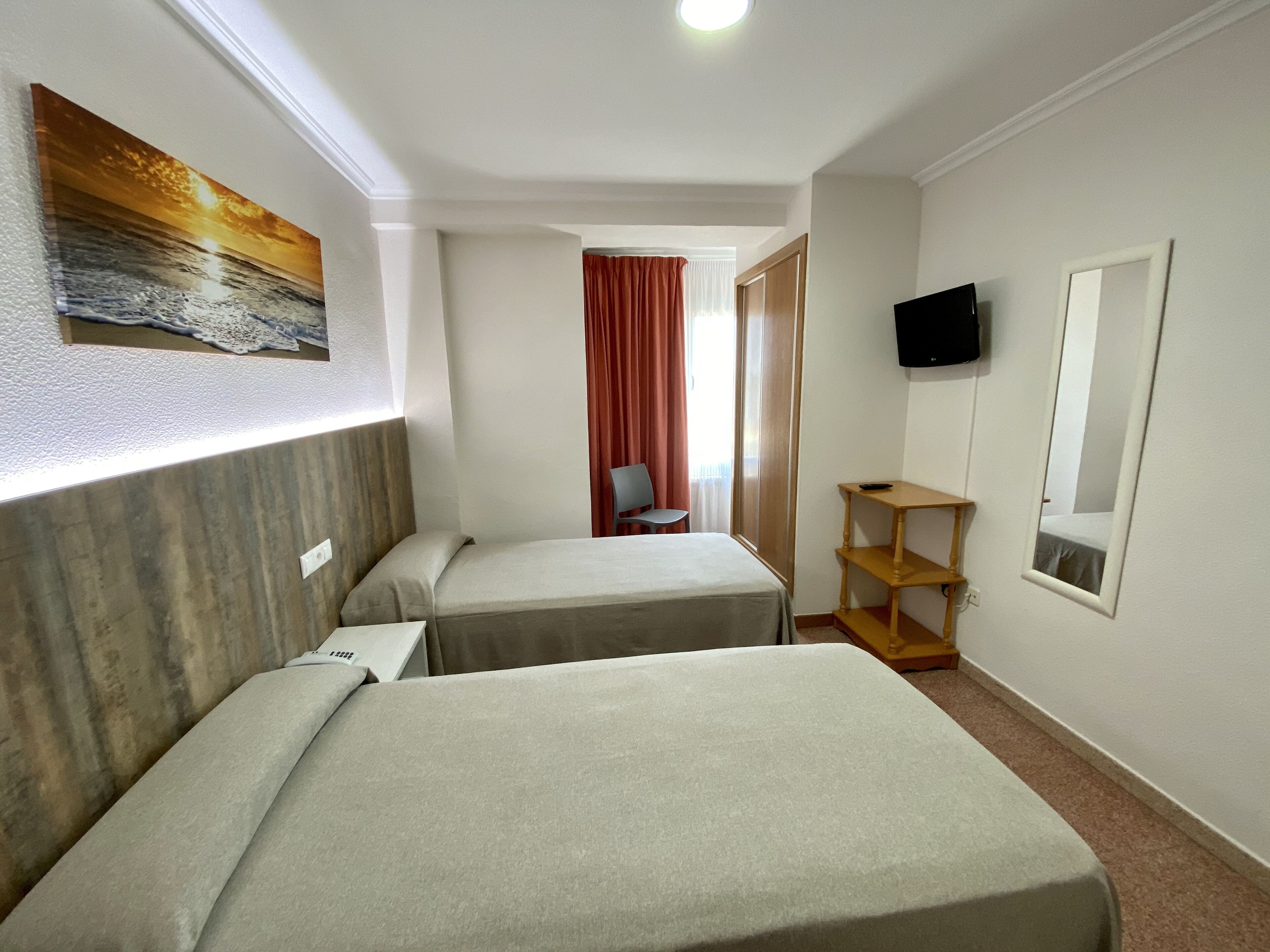 Habitación de hotel con dos camas, televisión, espejo y un cuadro en la pared.