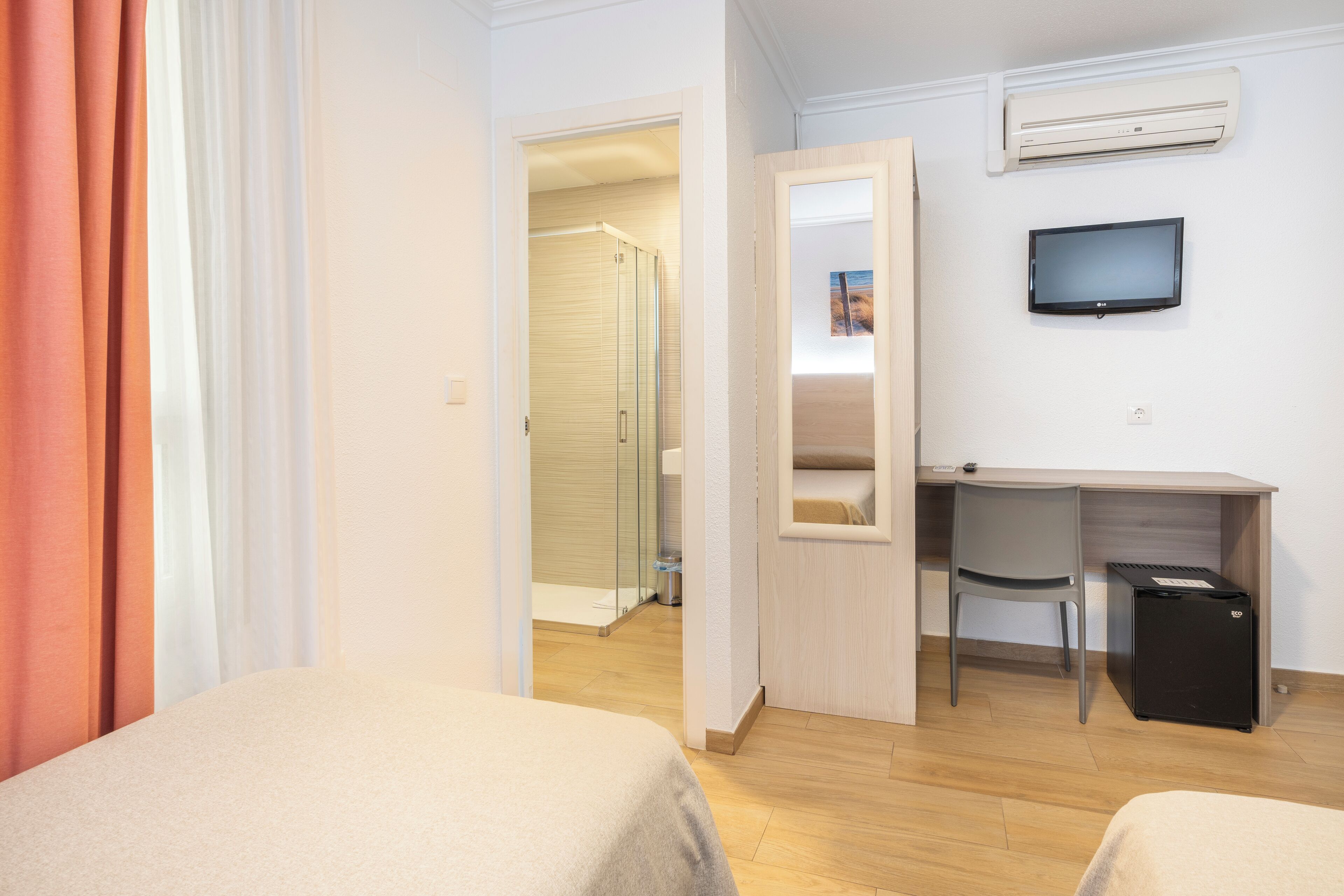 Una camera d'albergo con due letti, una scrivania con una sedia, una TV e un condizionatore d'aria.