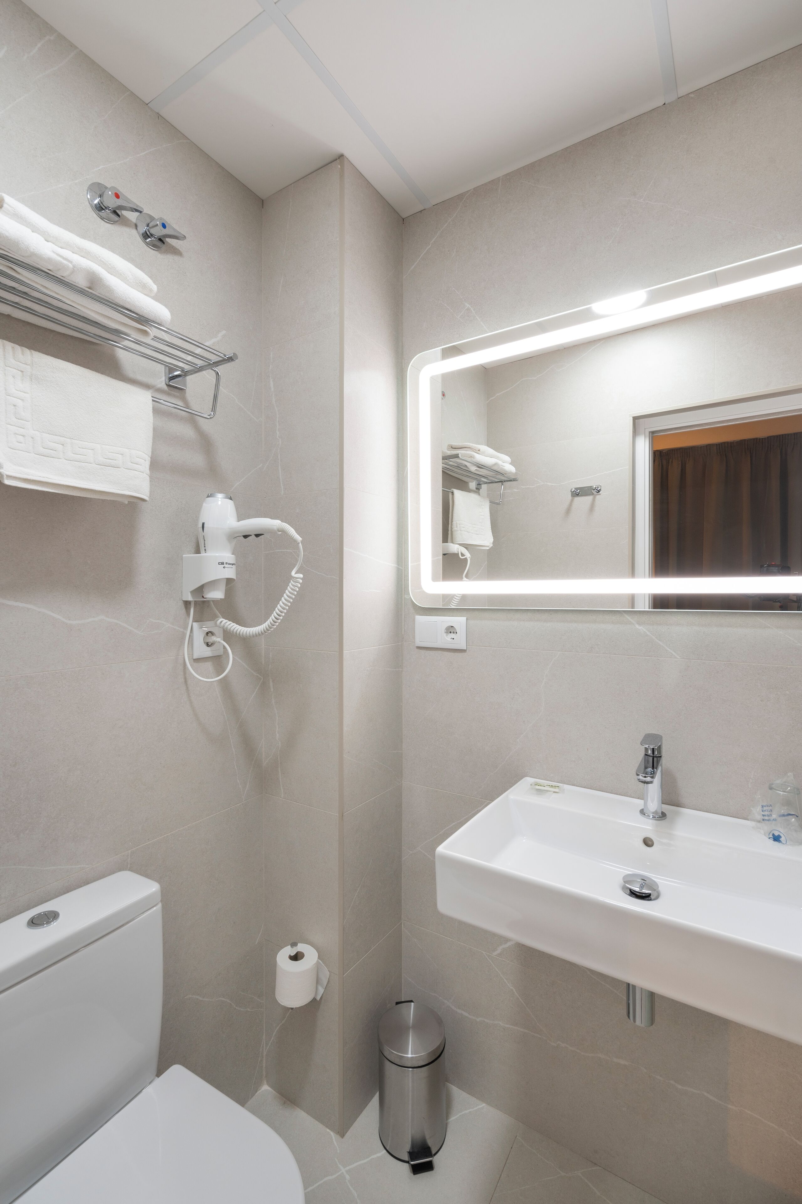 A modern bathroom with a toilet, sink, and hairdryer mounted on the wall.