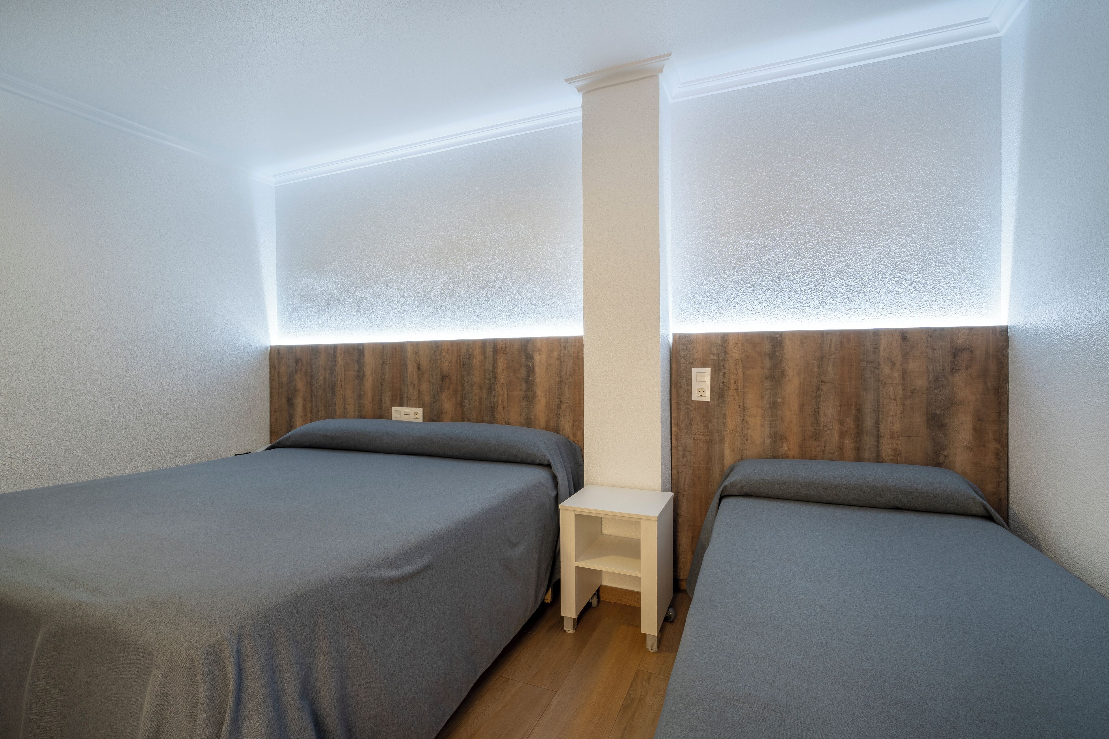 A room with two single beds, a small bedside table, and a wooden headboard.