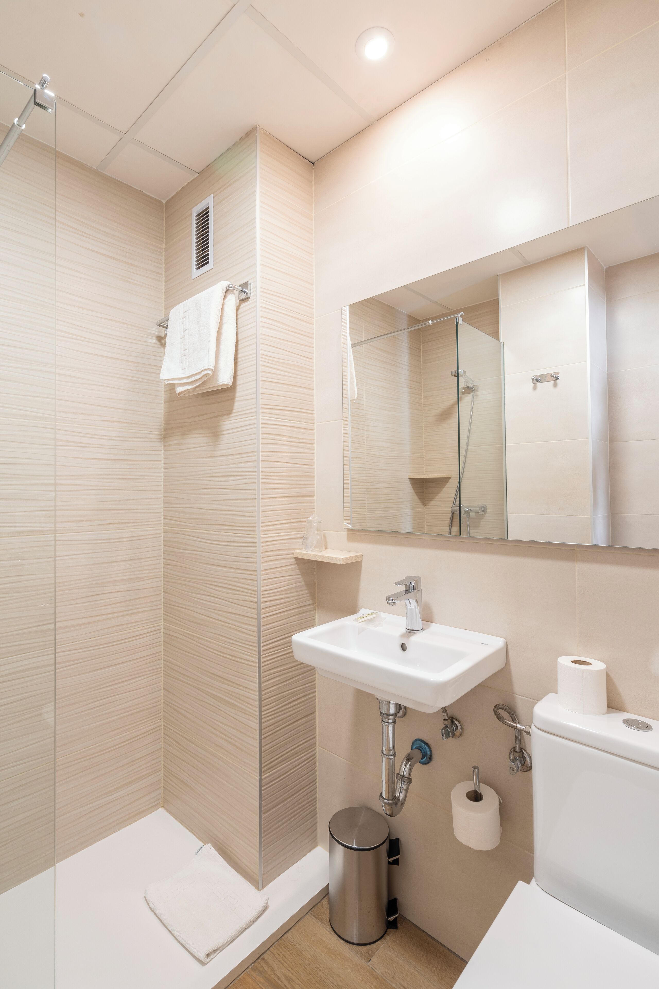 Een moderne badkamer met een douche, wastafel, toilet en spiegel.