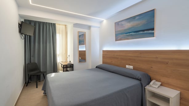 Hotellihuone, jossa on sänky, työpöytä tuolilla, seinälle asennettu televisio, taulu ja yöpöydällä puhelin.