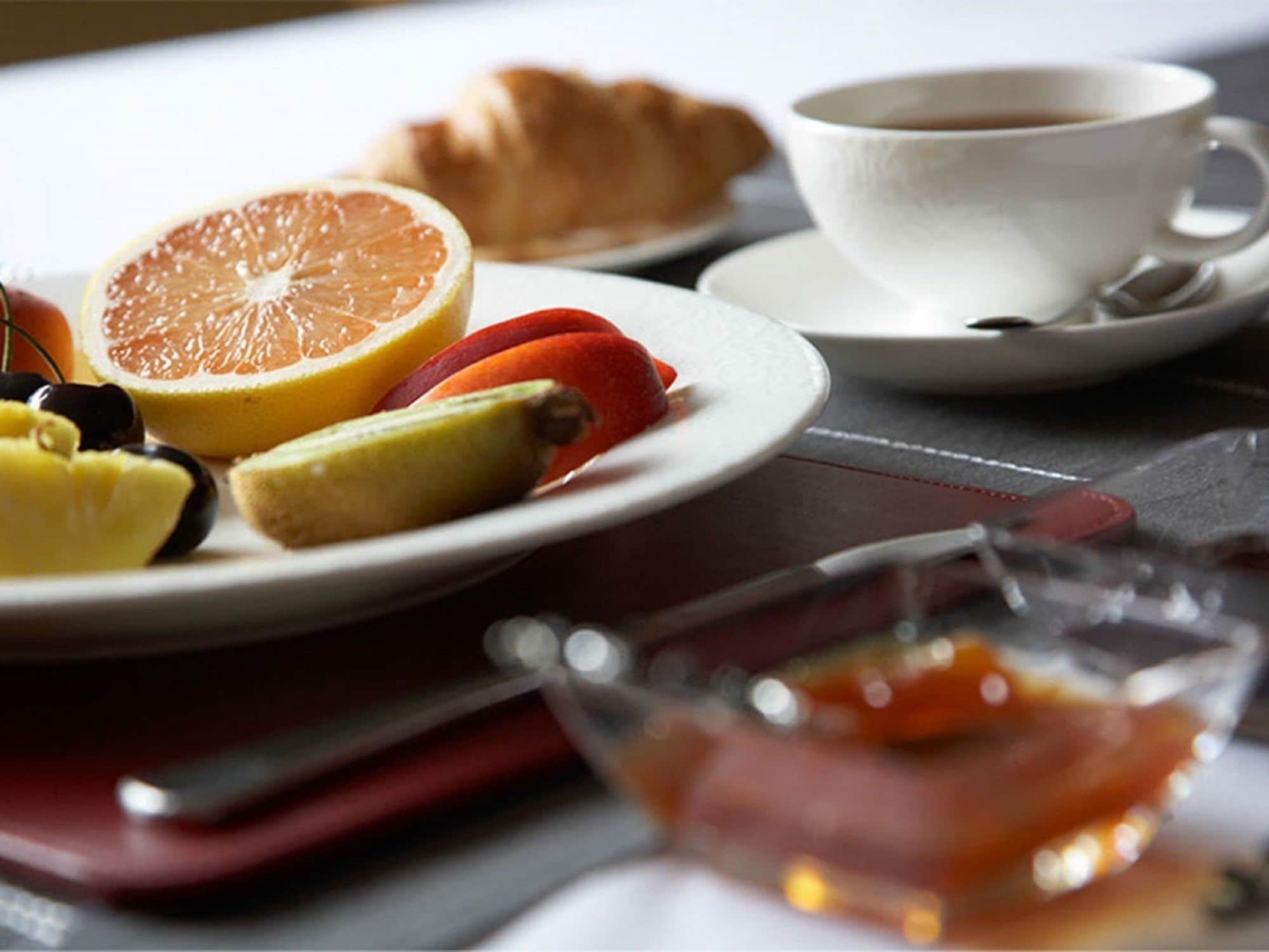 A breakfast setting with a plate of fruit, a croissant, and a cup of coffee.