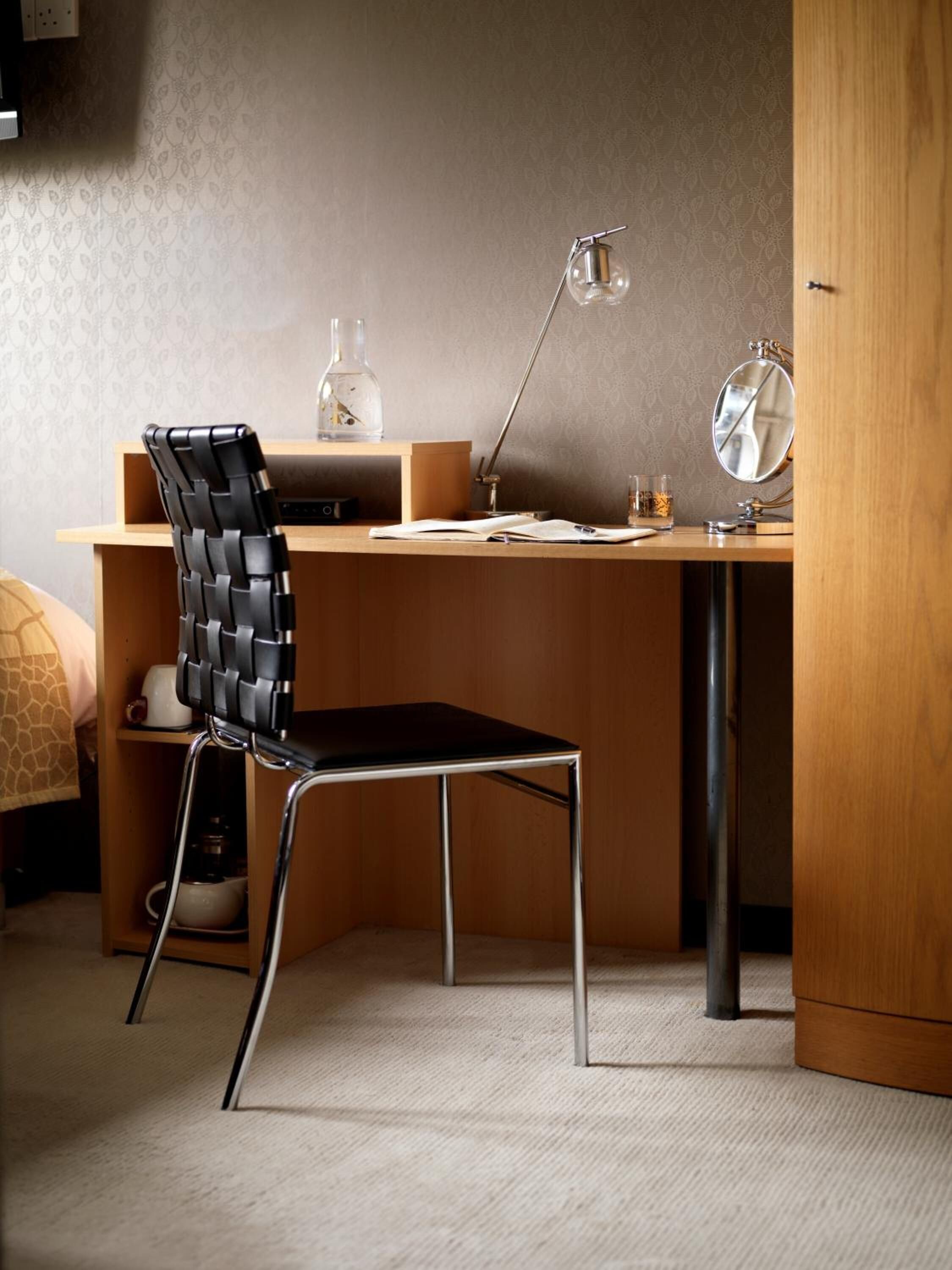 A modern study area with a wooden desk, a black and silver chair, a desk lamp, and a small mirror.