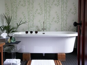 A bathroom with a freestanding bathtub, a sink with a mirror, a potted plant, and a towel rack.